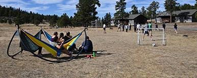 students playing soccer while others recline in hammocks and watch